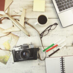 Writing tourism website copy with travel map, laptop, and camera on desk